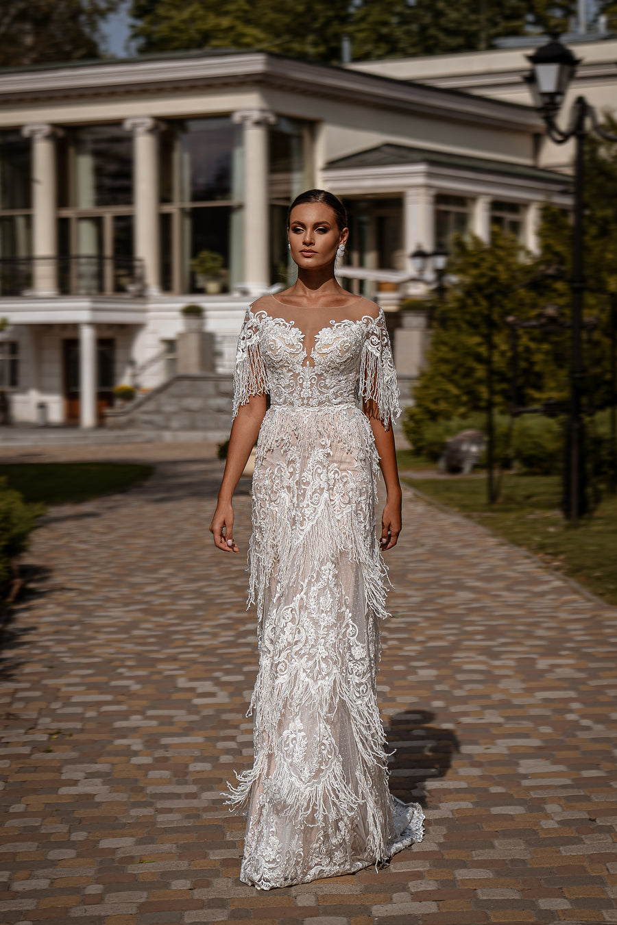 Ivory sheath wedding dress with an illusion neckline, beaded fringe sleeves, and a trailing hem