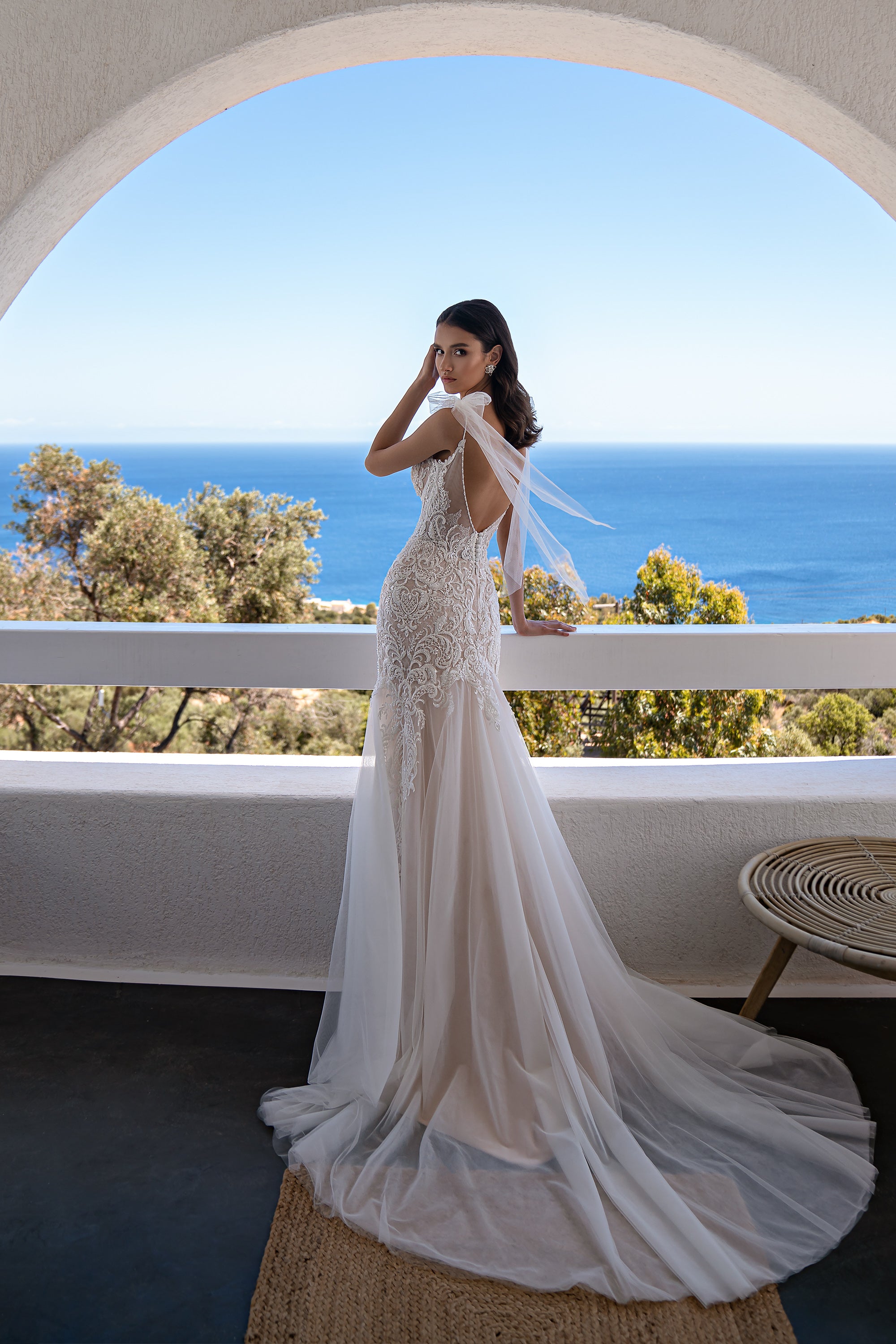 Side view of an ivory mermaid wedding dress with an open back, sheer shoulder drapes, and a long train