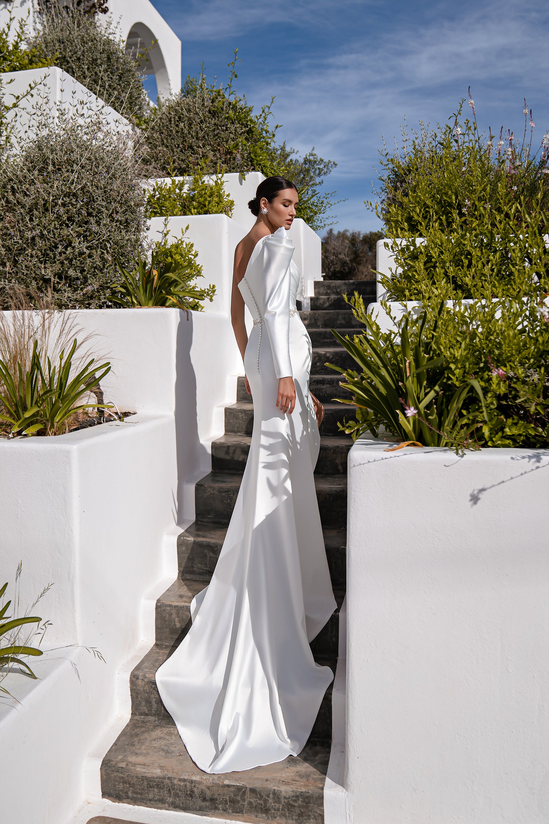 White wedding dress with an asymmetrical one-shoulder neckline, fitted skirt, and long flowing train