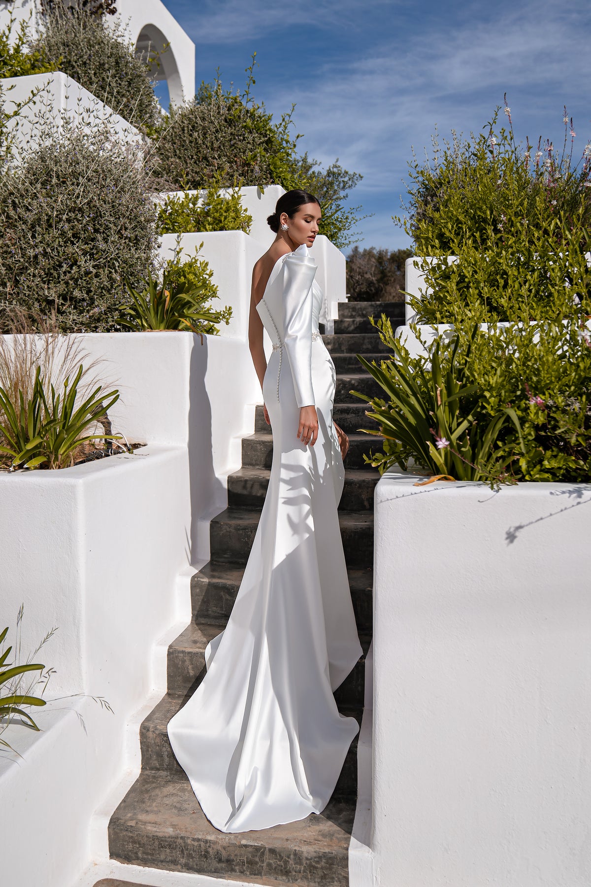 White wedding dress with an asymmetrical one-shoulder neckline, fitted skirt, and long flowing train