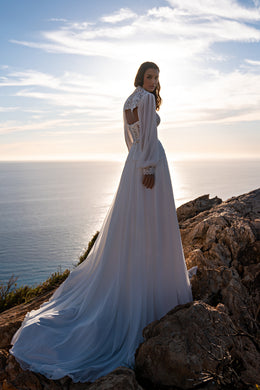 Open-back ivory wedding dress with a lace shoulder yoke, long sheer sleeves, and a flowing train