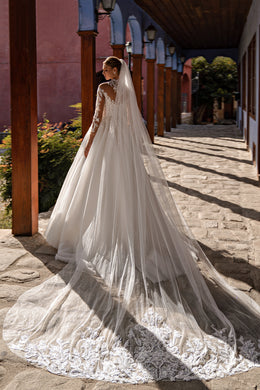 Long glittering wedding veil with an embroidered lace edge spread across the ground behind the gown