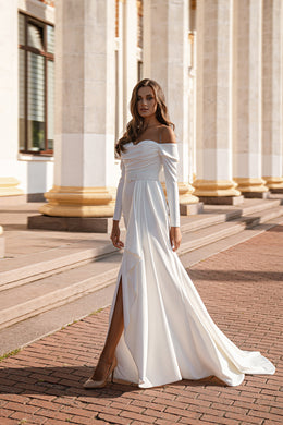 White wedding dress with an off-the-shoulder neckline, long sleeves, thigh-high slit, and sweeping train