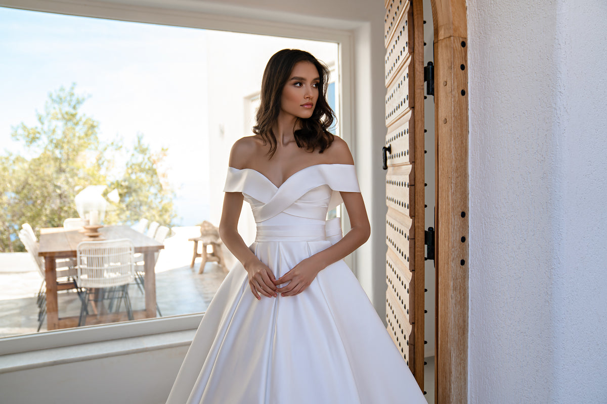 White satin wedding dress with an off-the-shoulder sweetheart neckline and pleated full skirt