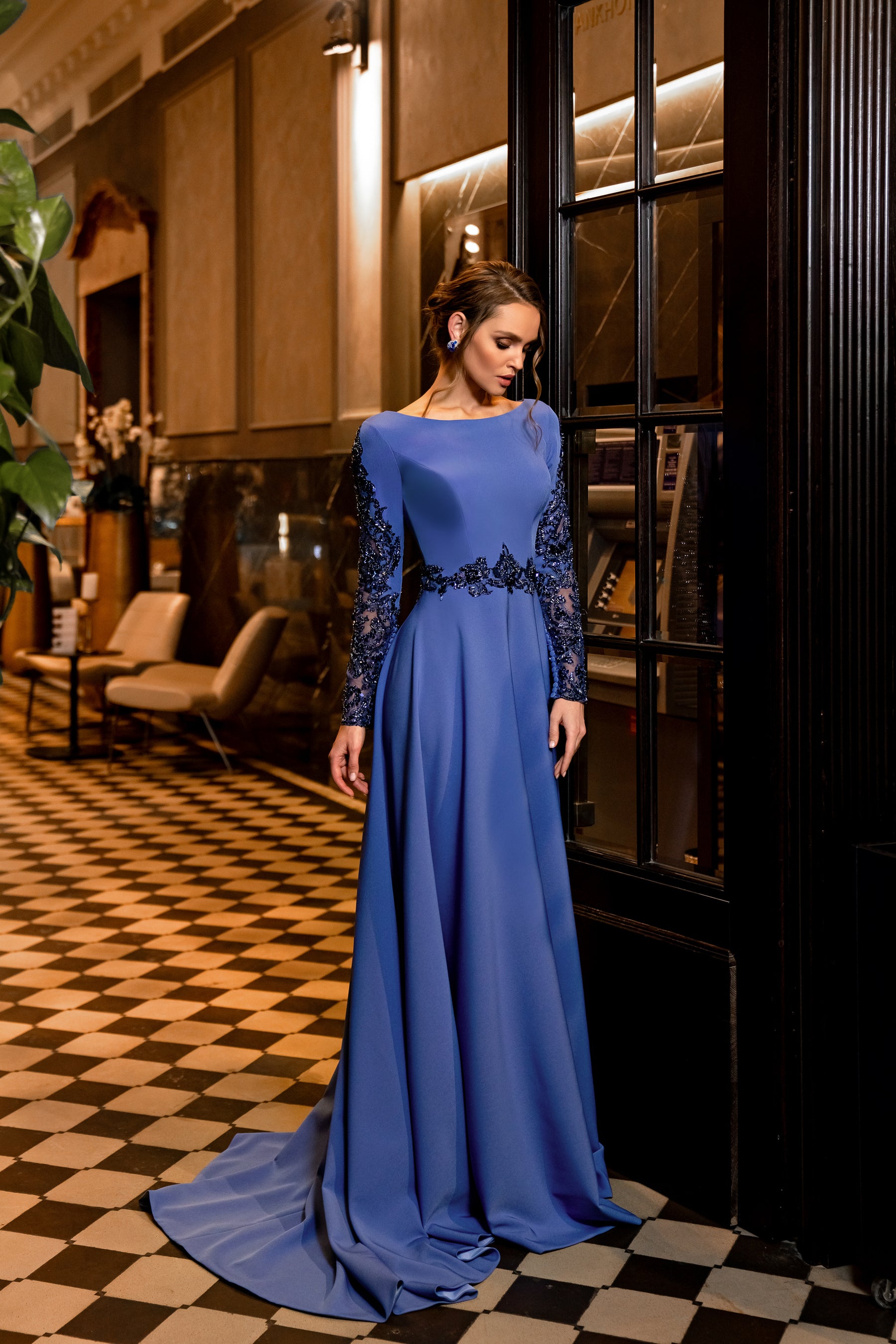 Sapphire evening dress with a bateau neckline, embellished long sleeves, beaded waist, and trailing hem