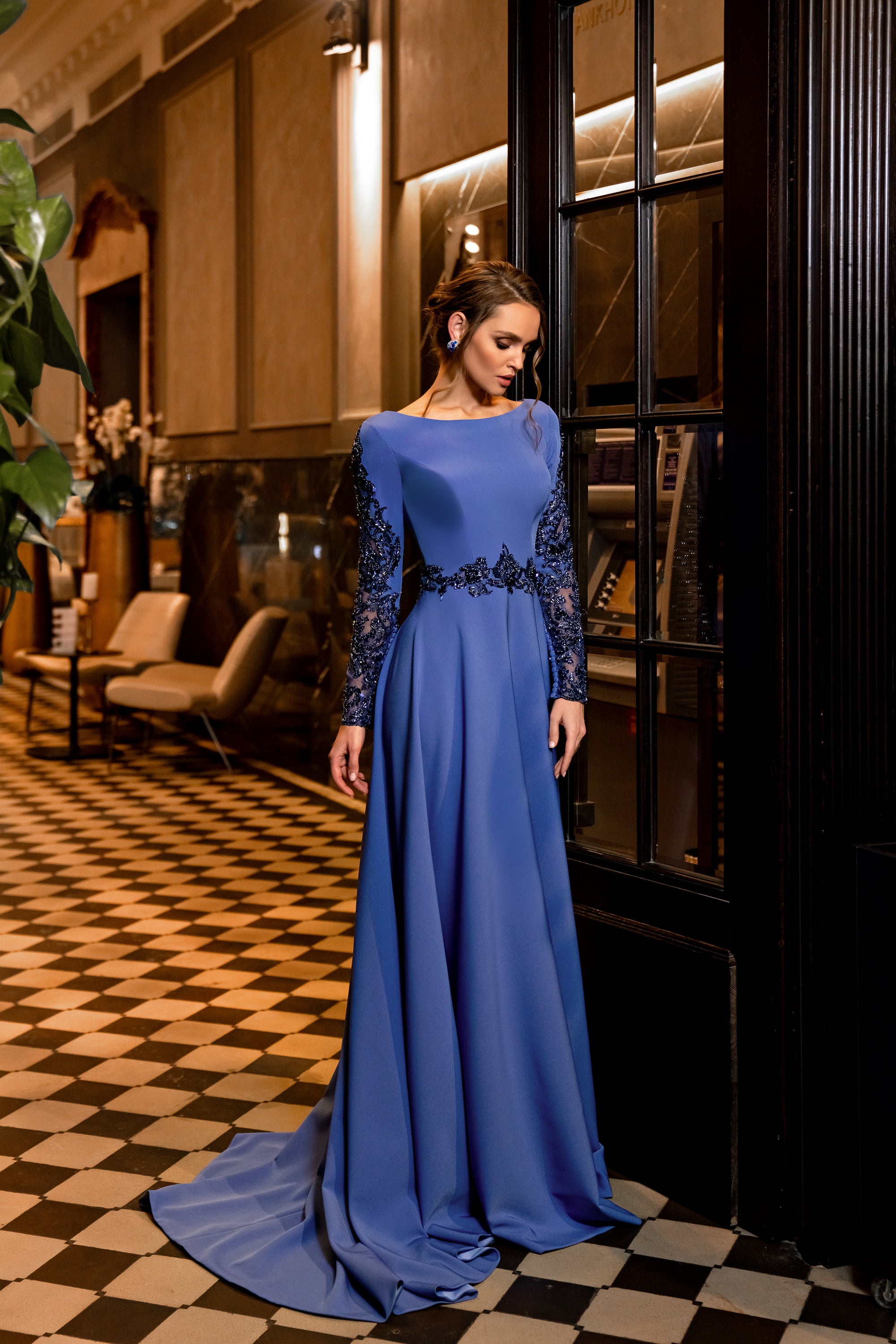 Sapphire evening dress with a bateau neckline, embellished long sleeves, beaded waist, and trailing hem