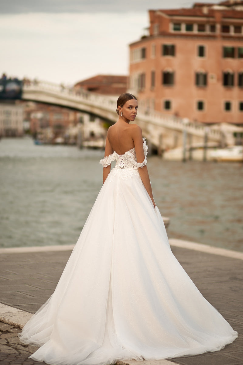 Open low-back wedding dress with off-the-shoulder lace sleeves, full A-line skirt, and long train