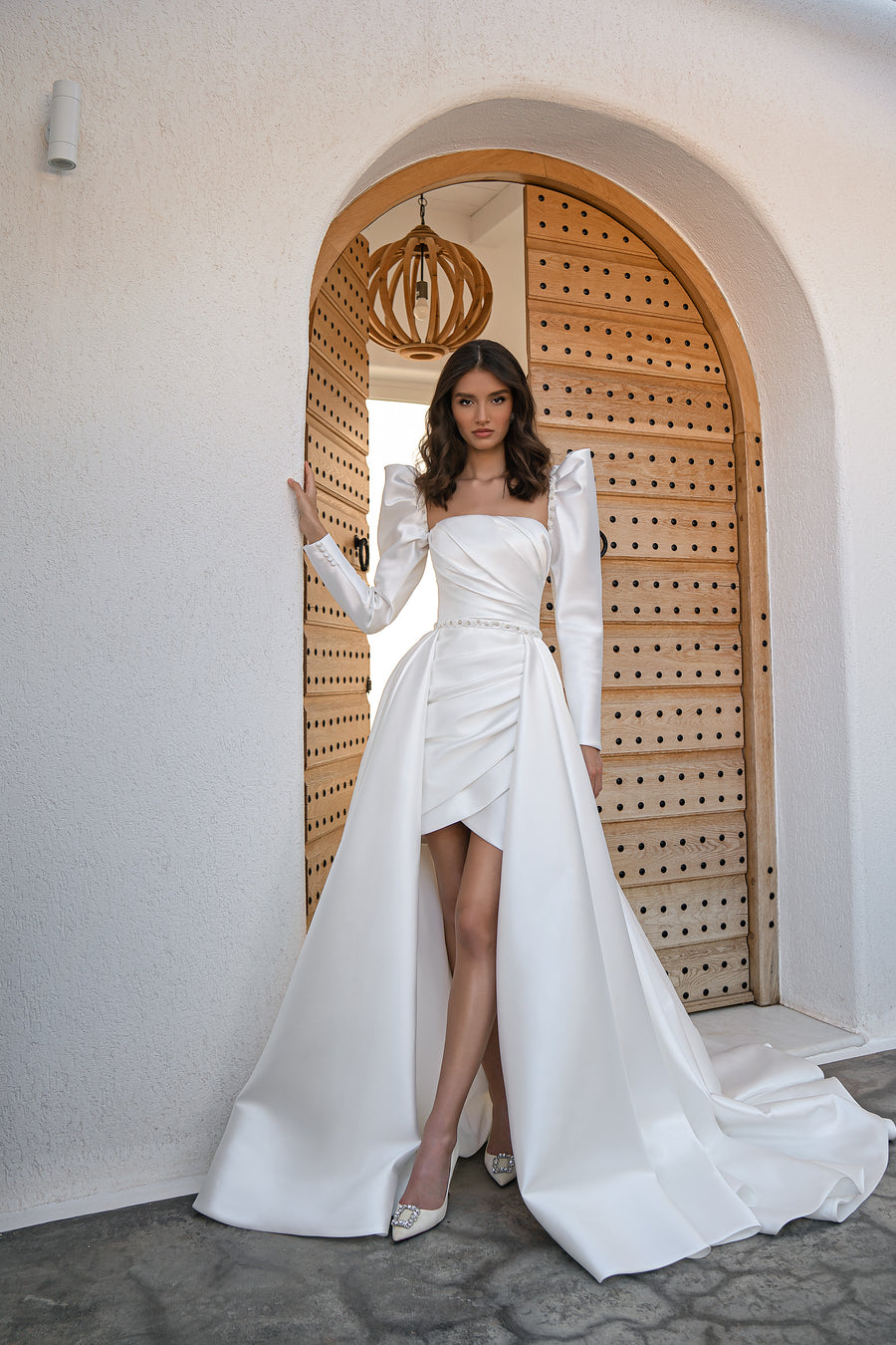 White satin wedding dress with square neckline, long puff sleeves, ruched mini skirt, and detachable overskirt
