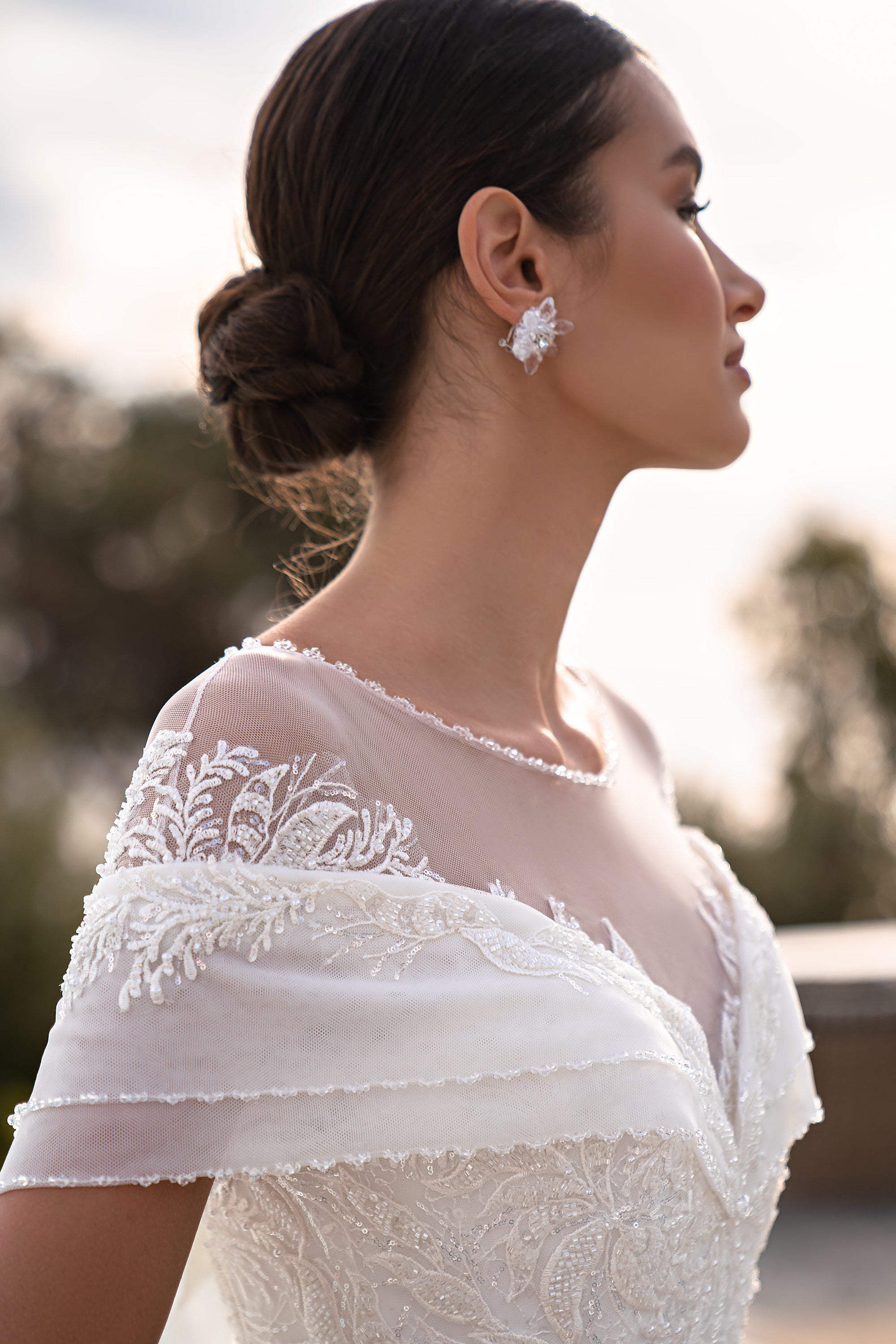 Close-up of the lace shoulder sleeve, sheer illusion neckline, and beaded bodice on a white wedding dress