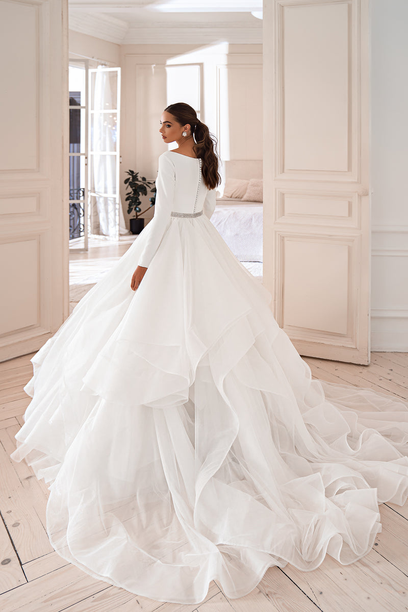 Back view of a white wedding dress with a sweeping full skirt and cascading ruffled train