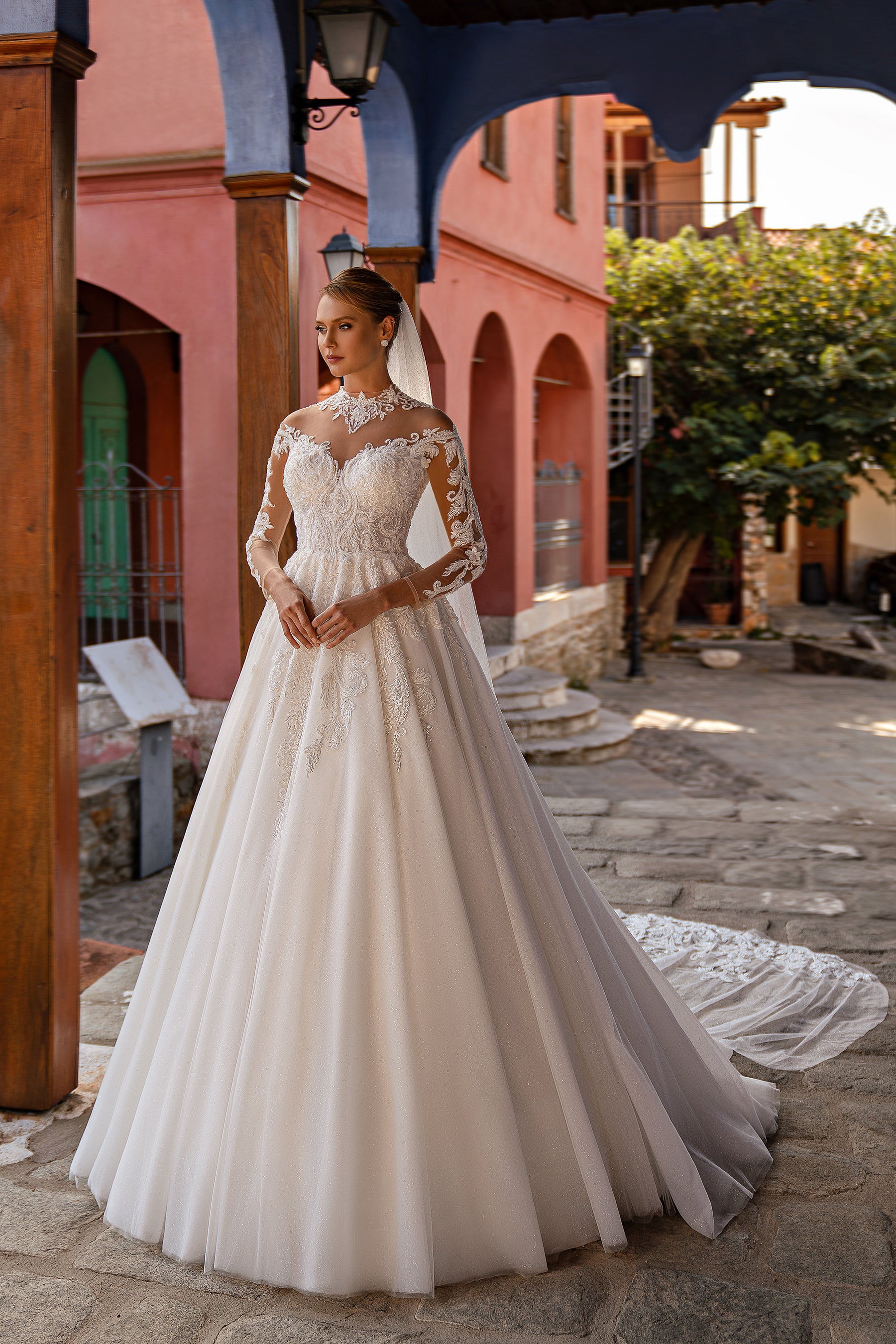 Sheer sparkling wedding veil draped over a long-sleeved lace bridal gown and extending into a train