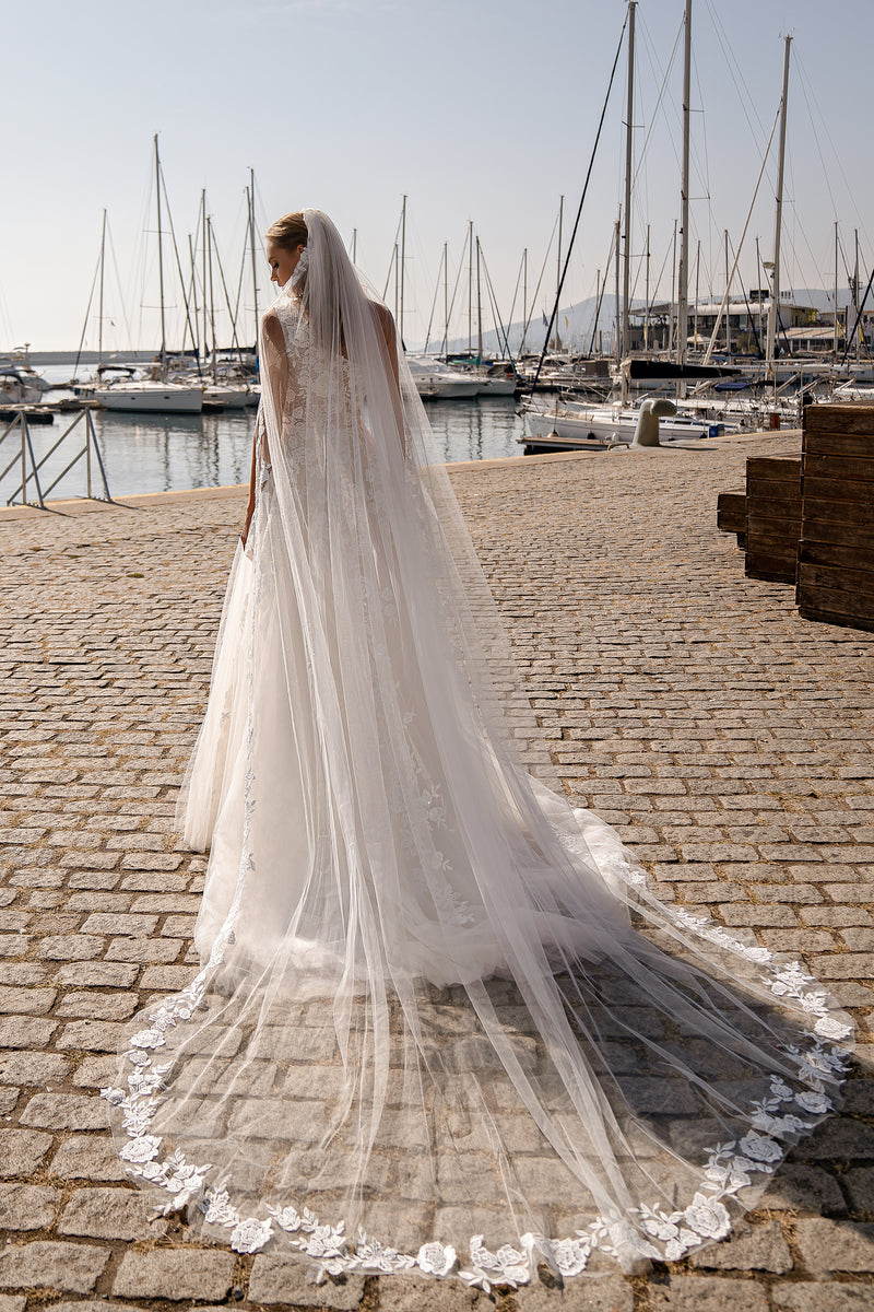 Ivory wedding dress shown from behind with a long, sheer train and scalloped floral lace trim