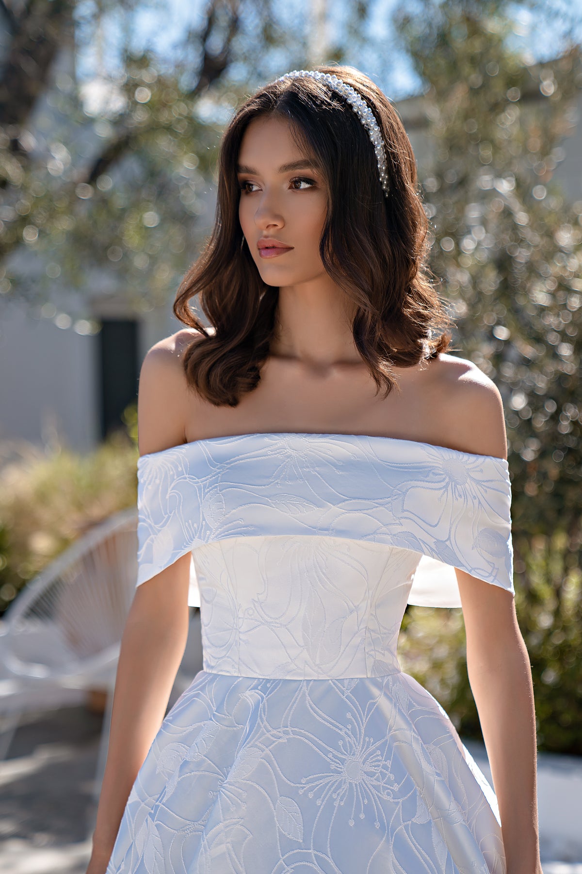 Close-up of an ivory wedding dress with an off-the-shoulder neckline and floral-patterned bodice