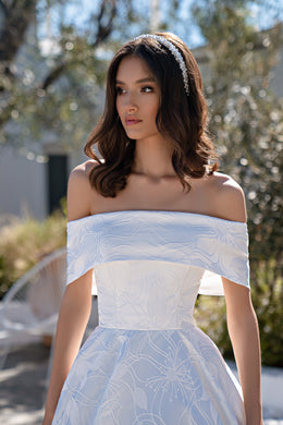 Close-up of an ivory wedding dress with an off-the-shoulder neckline and floral-patterned bodice