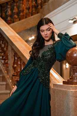 Deep teal evening dress with a sheer neckline, jeweled embroidered bodice, and gathered flowing skirt