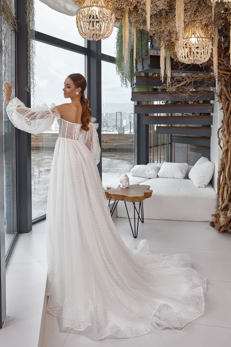 Back view of an ivory wedding dress with an exposed upper back, sheer sleeves, fitted bodice, and long flowing train
