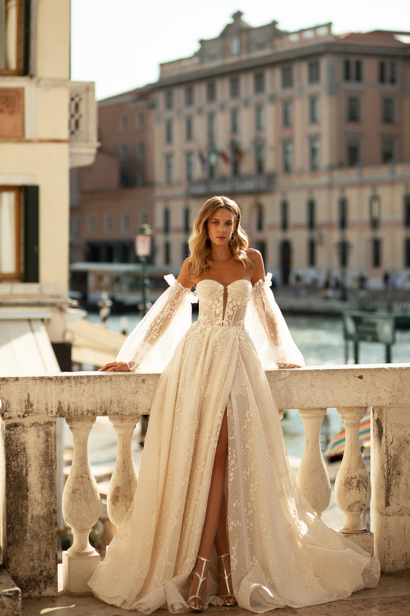 Ivory wedding dress with a sweetheart bodice, sheer floral lace sleeves, flowing A-line skirt, and train