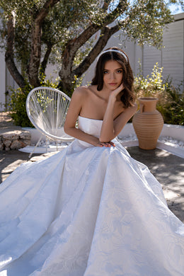 Ivory wedding dress close-up showing an off-the-shoulder bodice and flowing floral-patterned skirt