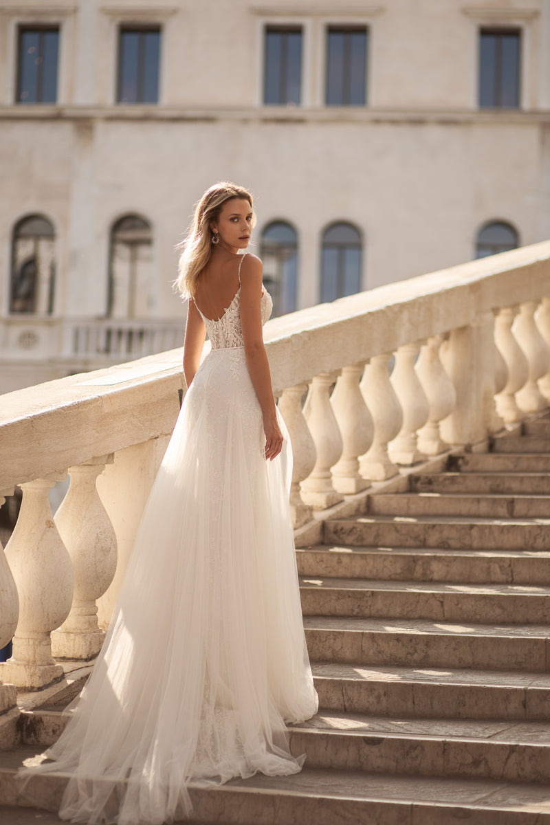 Open-back ivory wedding dress with slender straps, lace detailing, and a softly flared skirt with train