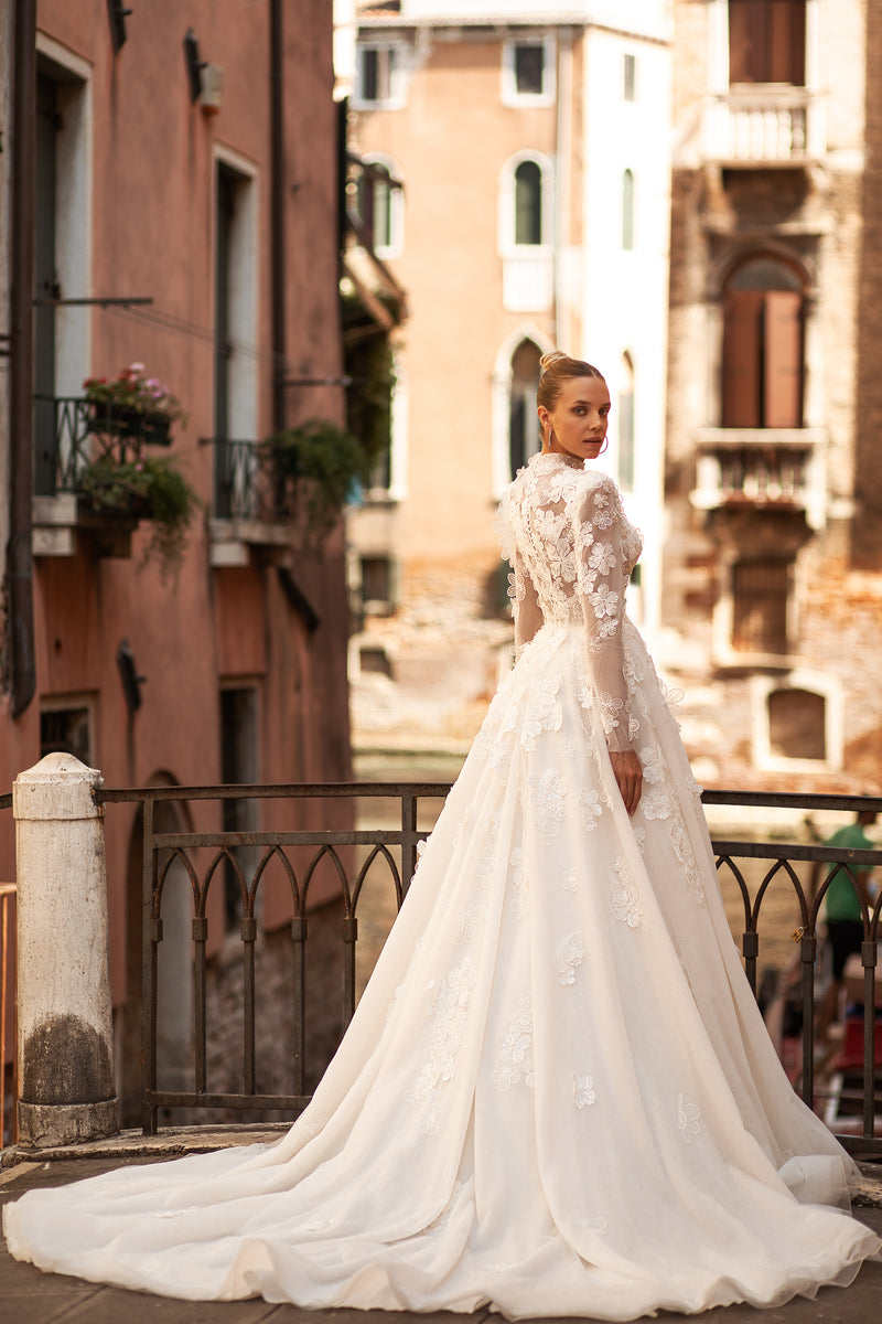 Side view of an ivory wedding dress showing its full A-line skirt, long lace sleeves, floral appliqués, and train