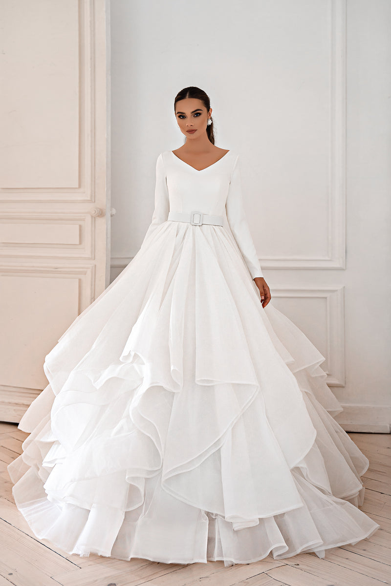 White long-sleeve V-neck wedding dress with a full ball gown skirt and layered ruffled train