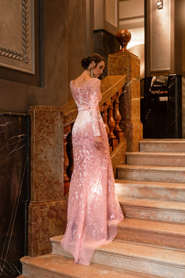 Blush pink evening dress showing an embellished back, long sleeves, mermaid silhouette, and flowing train