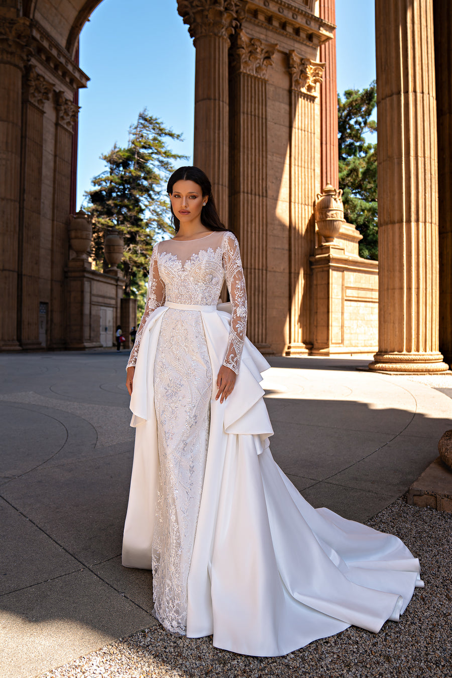 Ivory wedding dress with sheer lace sleeves, an embellished bodice, and detachable satin overskirt with train