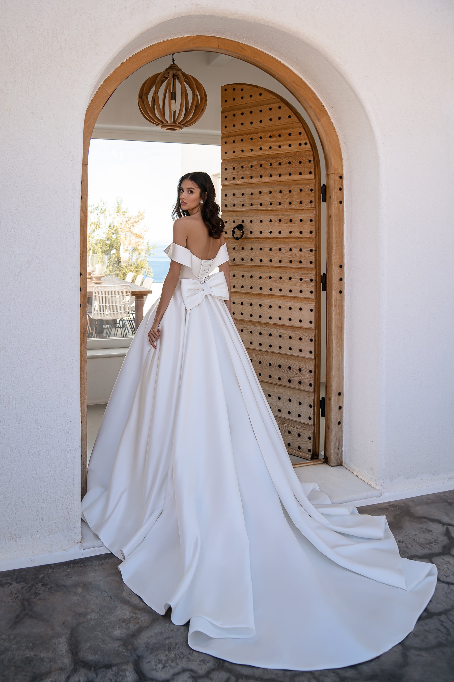 Back view of a white off-the-shoulder wedding dress with a large waist bow and sweeping train