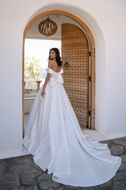 Back view of a white off-the-shoulder wedding dress with a large waist bow and sweeping train