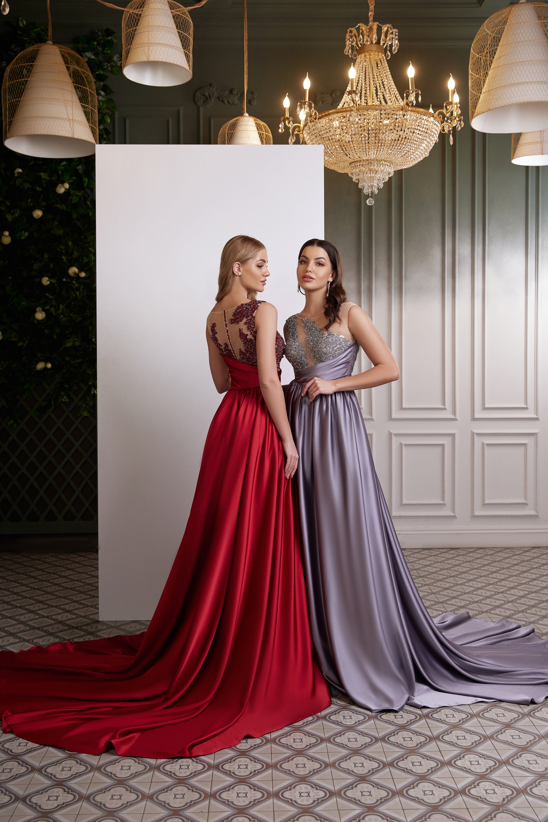 Three-quarter back view of red and lavender satin evening dress designs with floor-length skirts and trailing trains