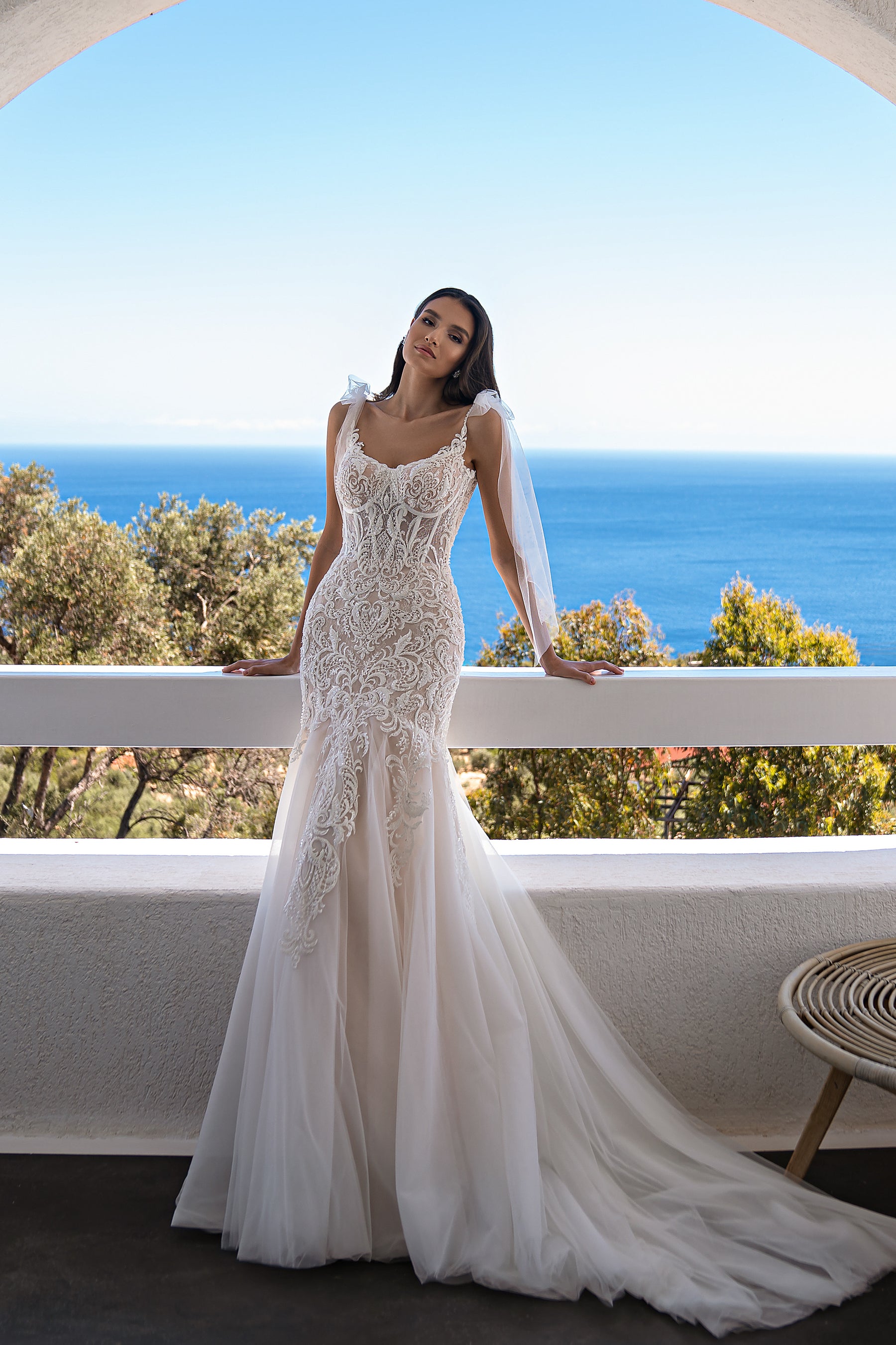 Ivory mermaid wedding dress with an ornate lace bodice, thin straps, sheer sleeves, and a flowing train