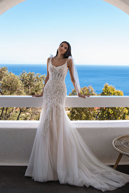 Ivory mermaid wedding dress with an ornate lace bodice, thin straps, sheer sleeves, and a flowing train