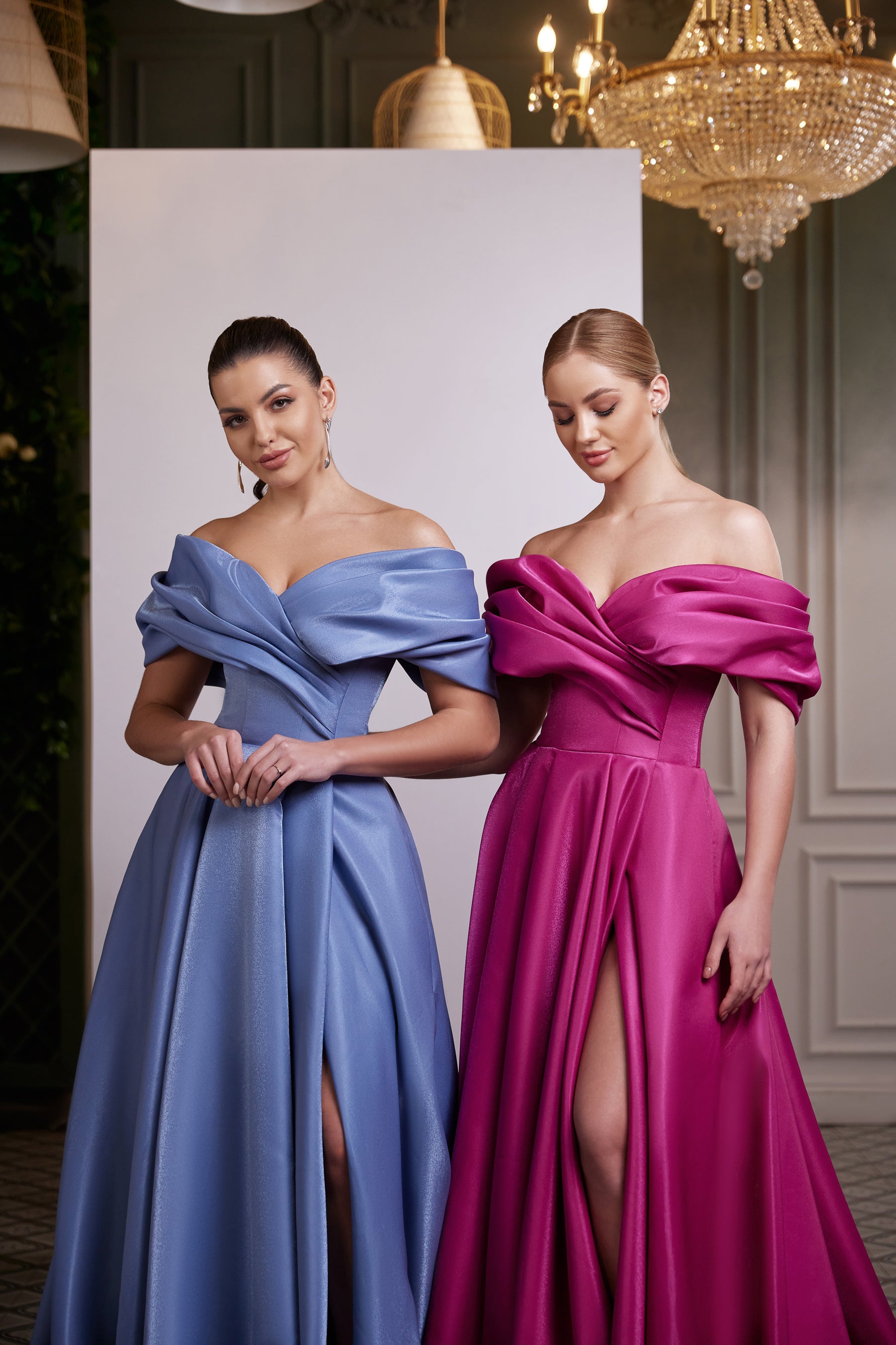 Close view of blue and magenta evening dresses with off-shoulder draping, fitted waists, and thigh-high slits