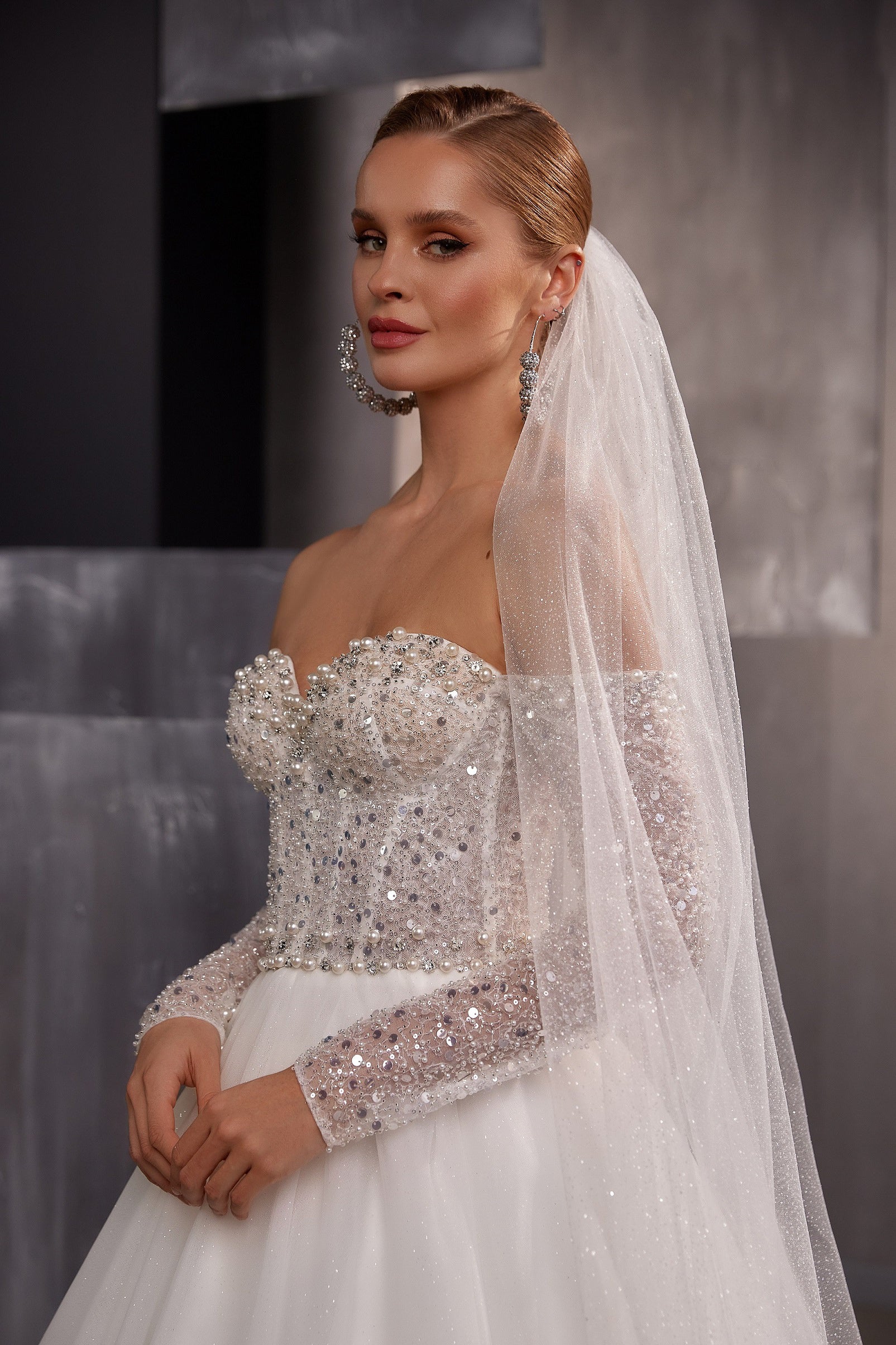 Sheer white sparkling wedding veil draped from a bridal updo and falling over the shoulder