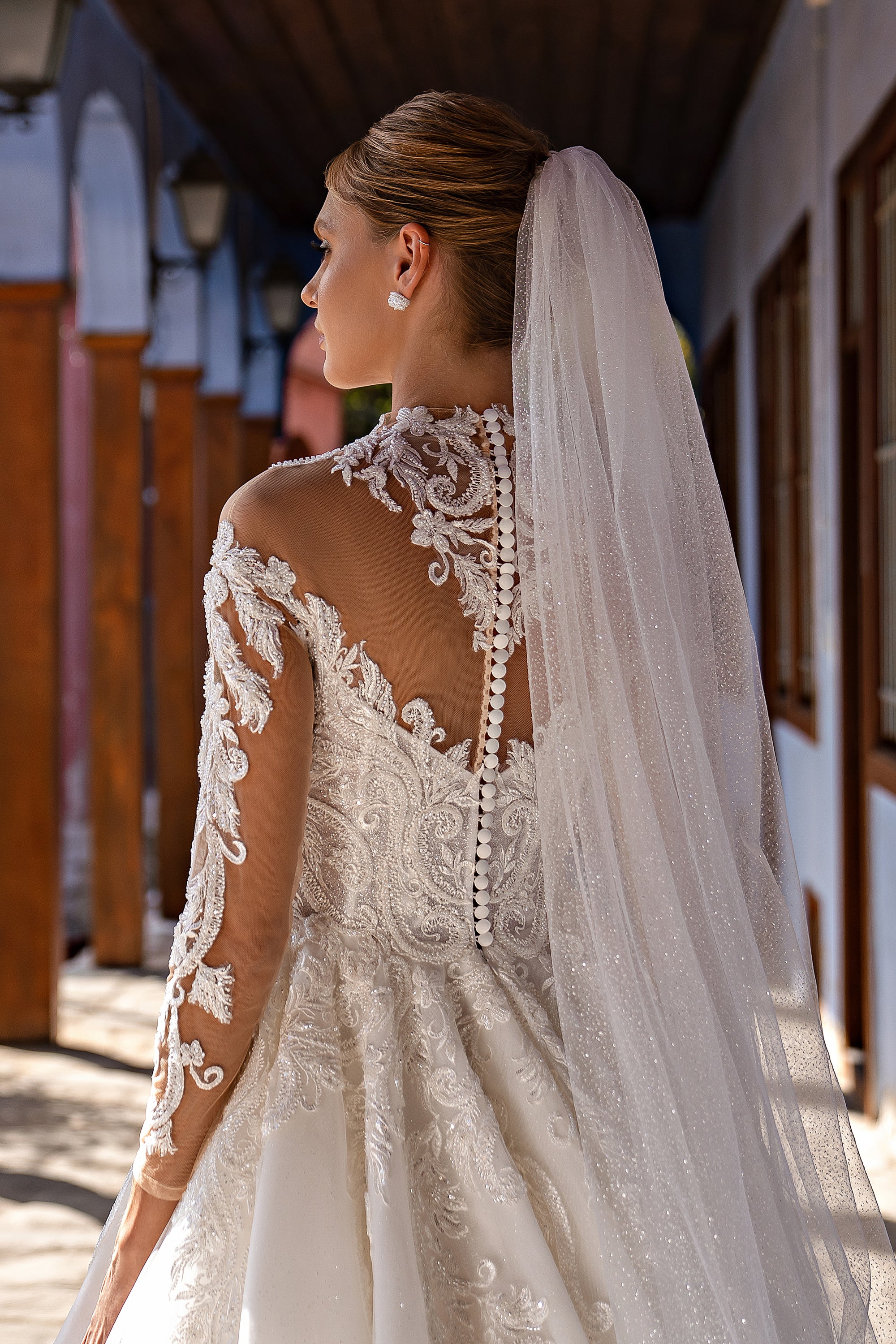 Close-up of a sheer dotted wedding veil attached at the updo and falling over the gown’s lace back