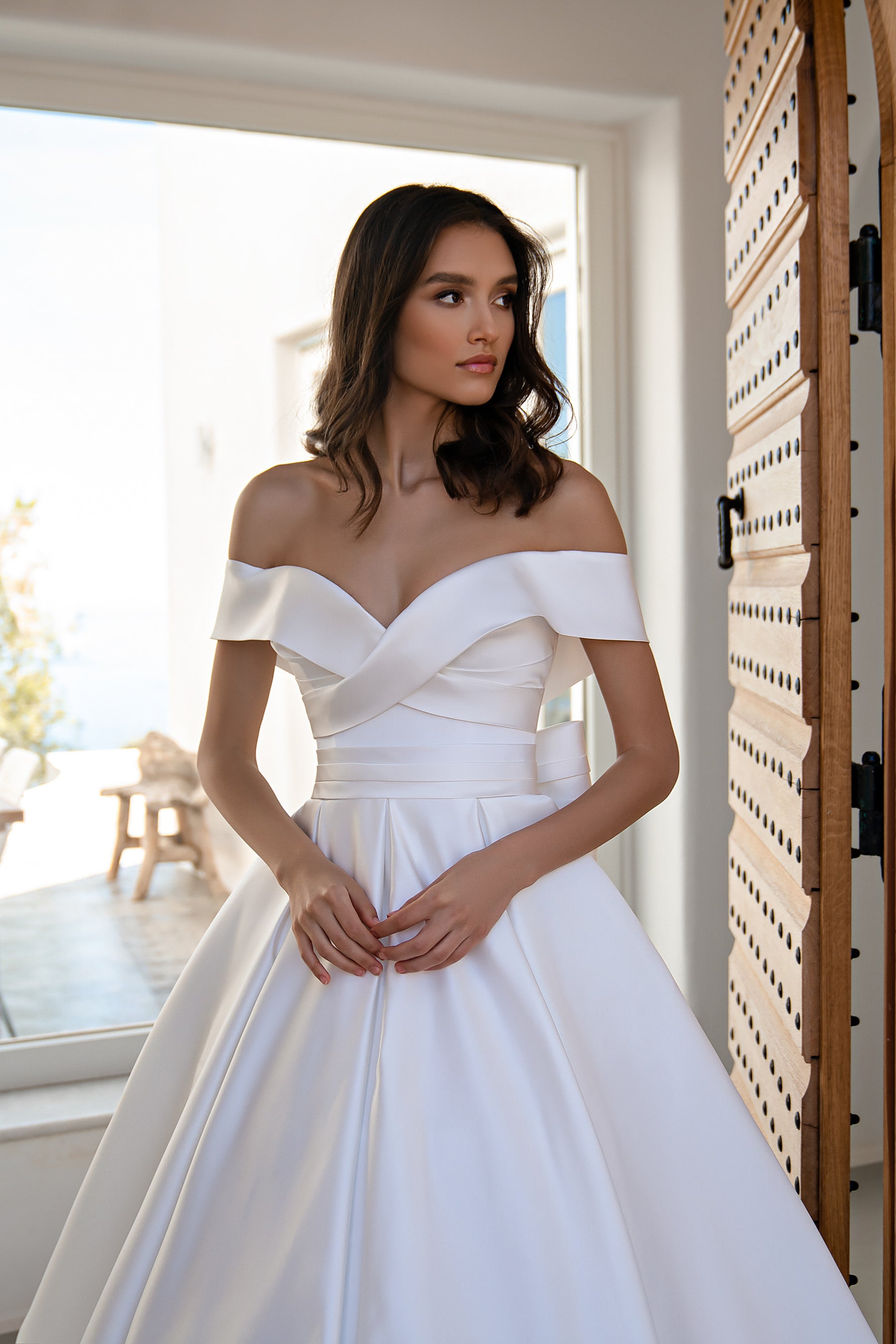 White wedding dress featuring an off-the-shoulder neckline, crossover bodice, and defined waist