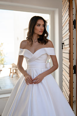White wedding dress featuring an off-the-shoulder neckline, crossover bodice, and defined waist