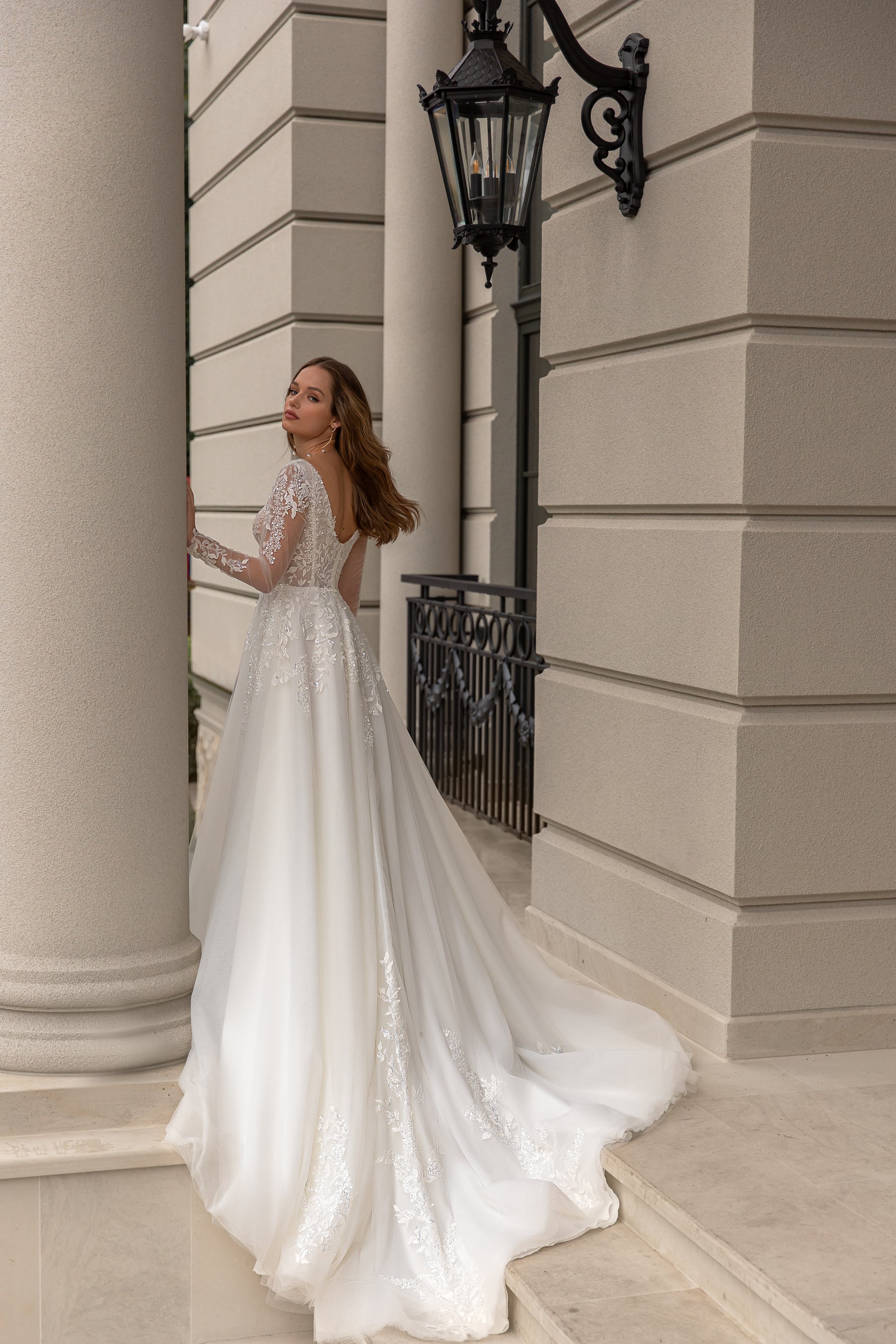 Rear three-quarter view of an ivory wedding dress with lace sleeves, an open back, floral appliqués, and train