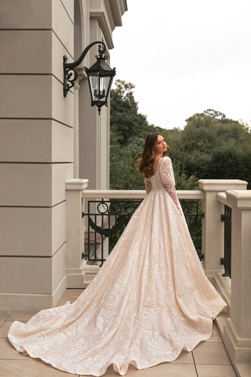 Ivory wedding dress shown from behind with a sweeping train and long sheer sleeves covered in sequined swirls