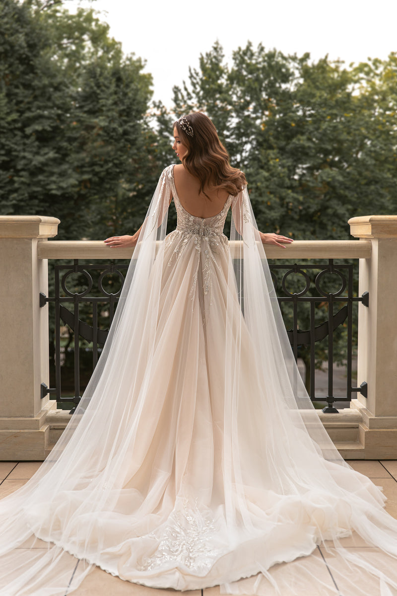Low open back on an ivory wedding dress with sheer draped sleeves and a long embellished train