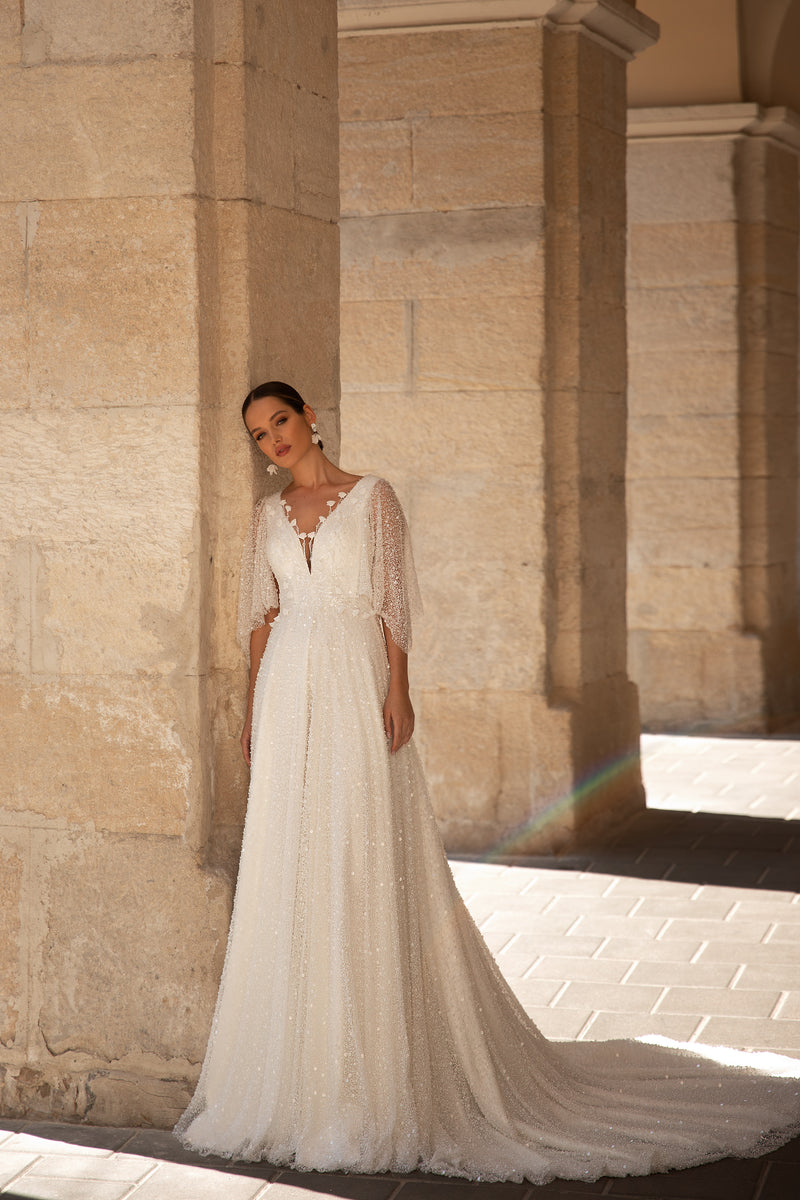 Ivory A-line wedding dress with a V-neckline, glittering fabric, sheer sequin sleeves, and a sweeping train