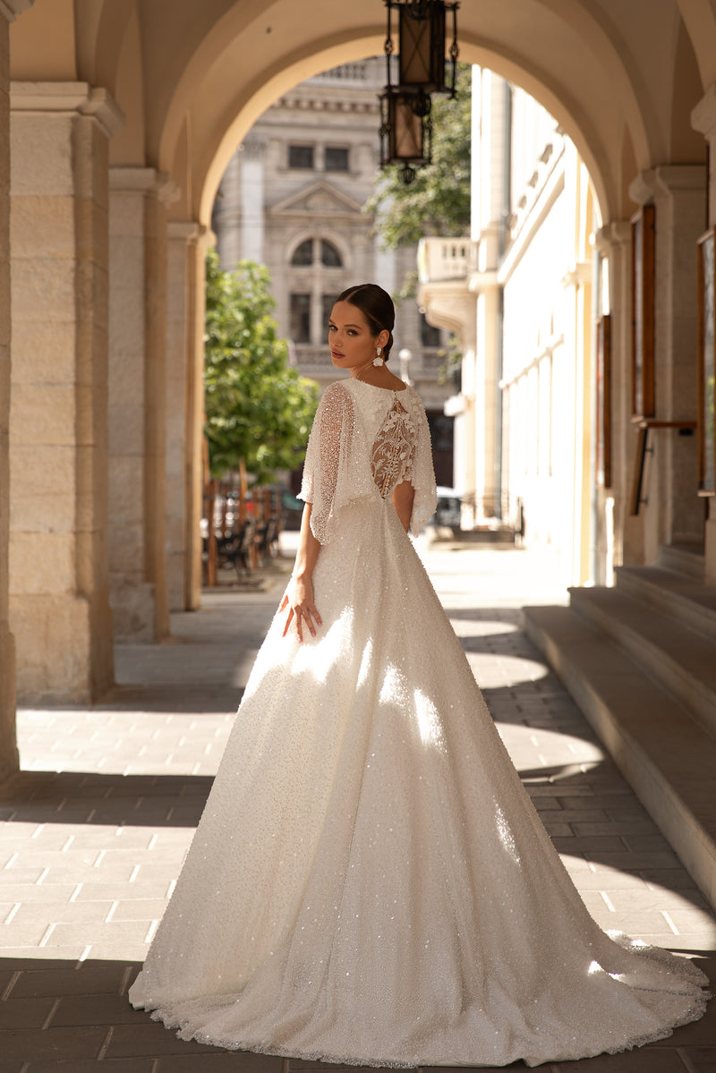 Ivory wedding dress with a sparkling beaded back, three-quarter sleeves, a full skirt, and a flowing train
