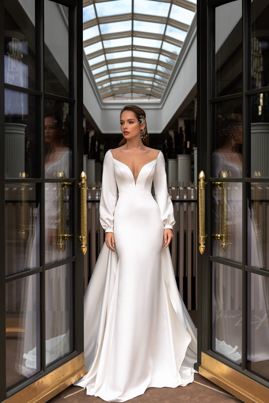 Ivory fit-and-flare wedding dress with a beaded deep V-neckline, long sleeves, and sweeping train