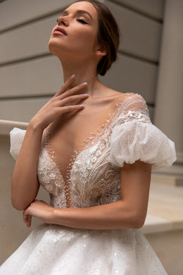 Close-up of an illusion V-neck wedding dress bodice with puff sleeves, sequins, and floral lace appliqués