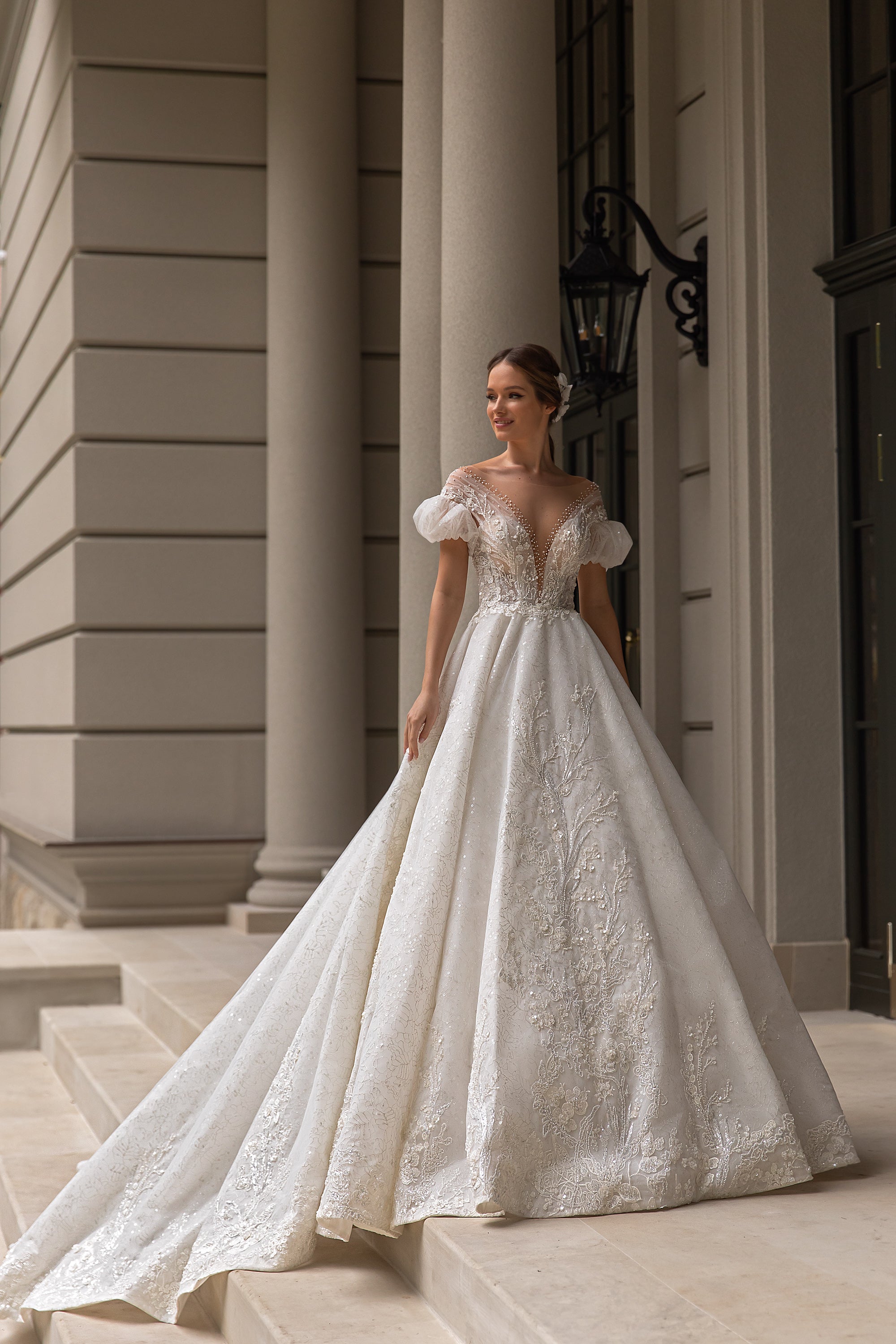 Ivory ball gown wedding dress with a deep V-neckline, puff sleeves, sparkling lace appliqués, and a long train