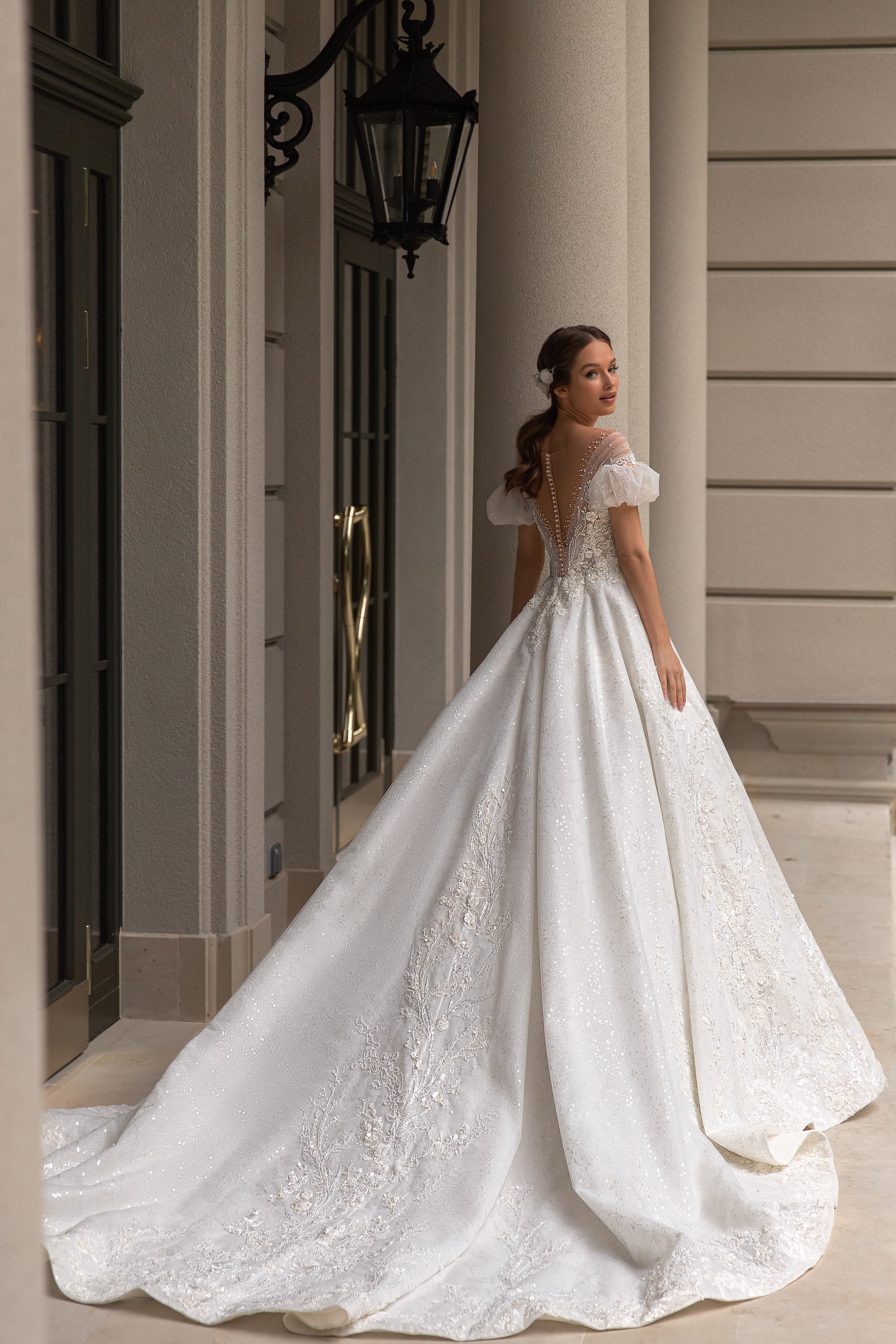 Open-back ivory wedding dress with short puff sleeves, shimmering lace appliqués, and a sweeping train