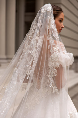 Close-up of a beaded back and puff sleeve beneath a sheer floral lace veil on a wedding dress