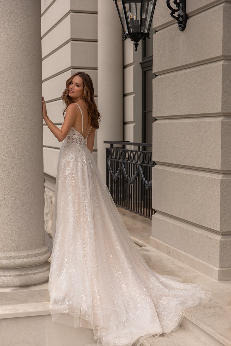Open-back ivory wedding dress with thin straps, sparkling tulle A-line skirt, and flowing train