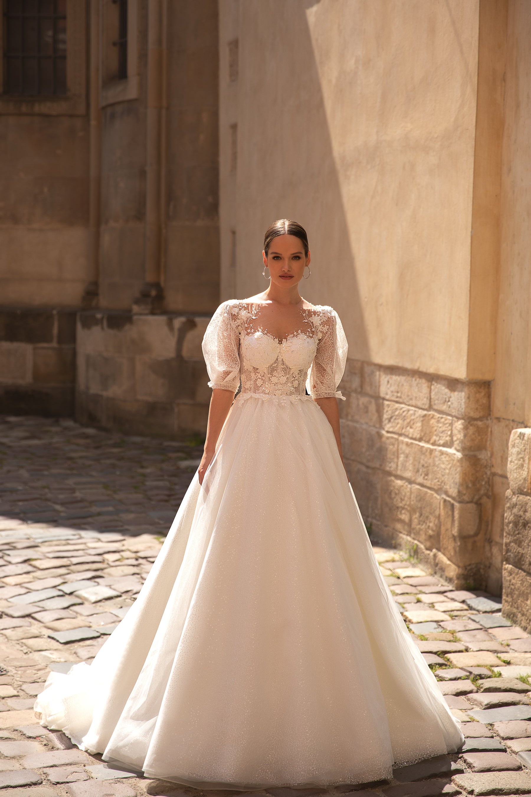 Ivory A-line wedding dress with a sparkling skirt, sheer puff sleeves, lace bodice, and court train