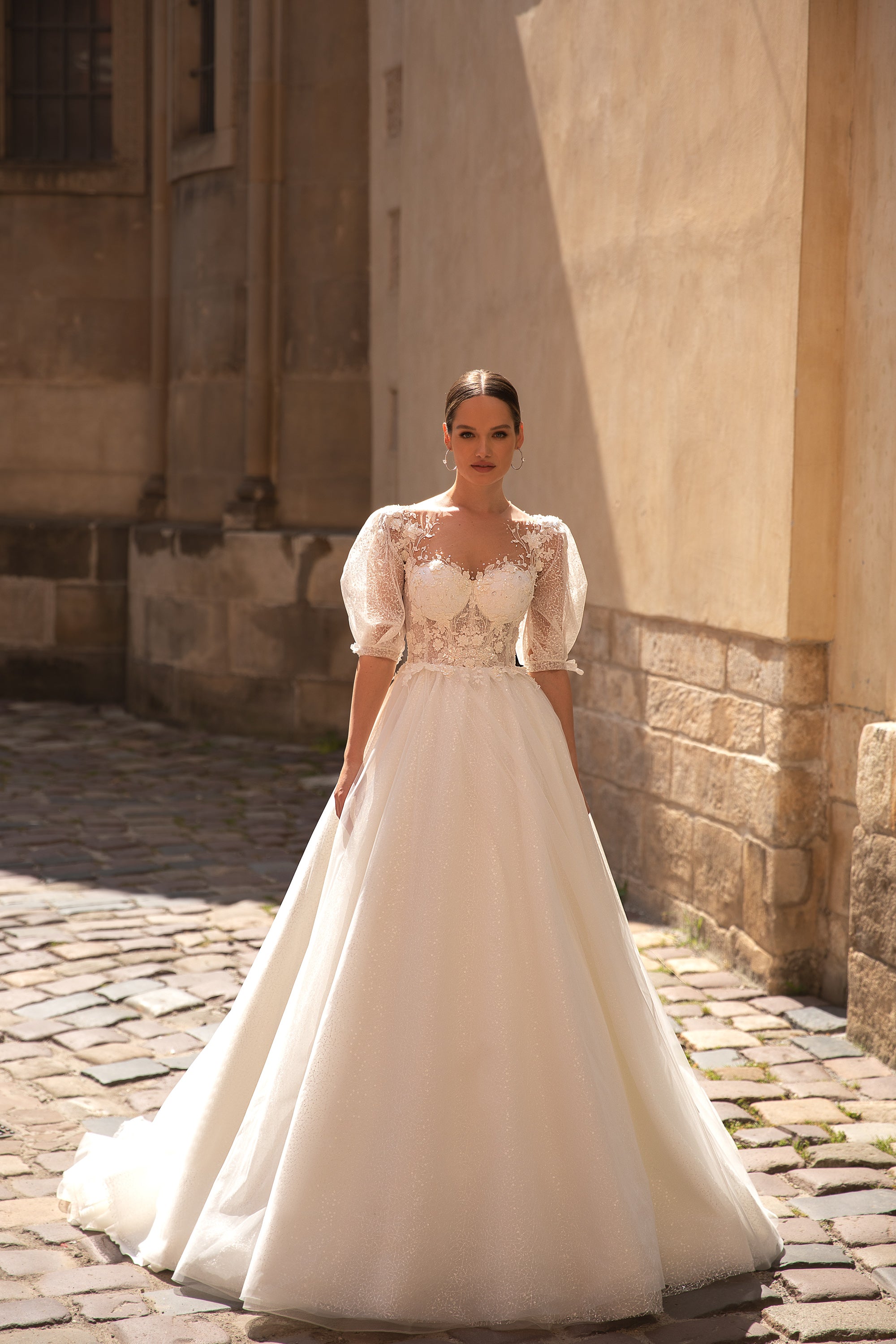 Ivory A-line wedding dress with a sparkling skirt, sheer puff sleeves, lace bodice, and court train